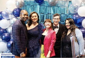 Five teen volunteers at a Texas fundraiser pose by blue-and-white balloon decor.