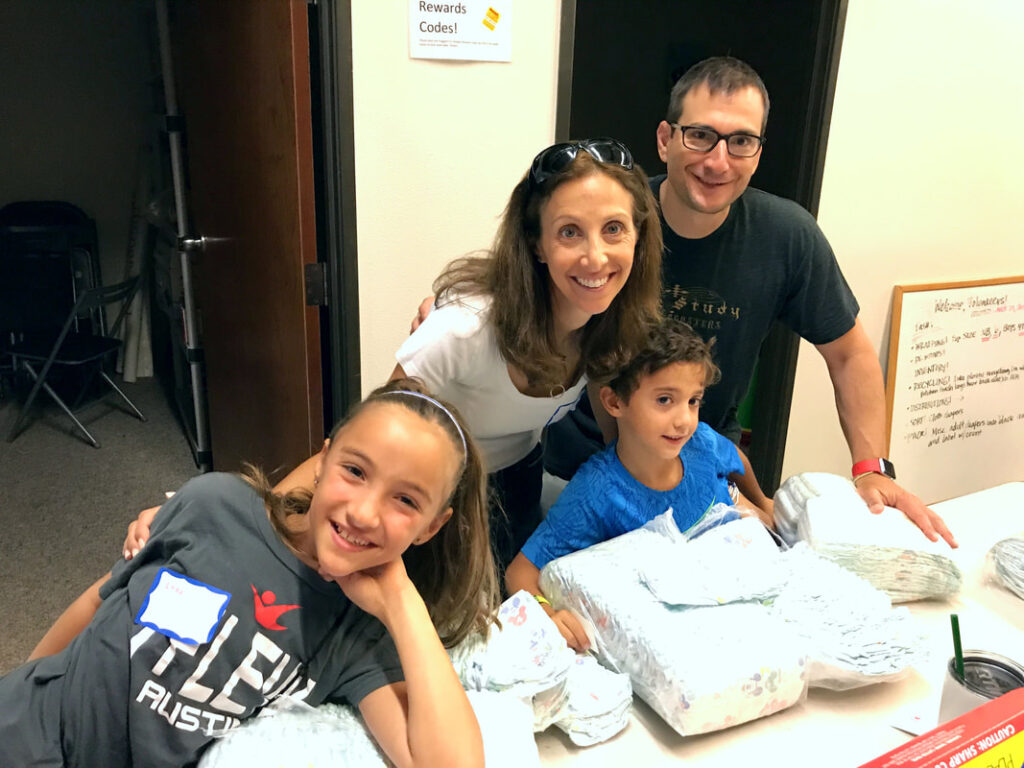 A family celebrates volunteering at a table of diapers for youth volunteer programs Texas.