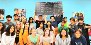 Teens pose indoors holding a sign promoting youth volunteer programs in Texas.