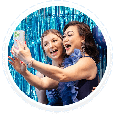 Two women in blue dresses take a selfie at a youth volunteer program event.
