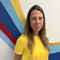 A teen volunteer in a yellow shirt stands before a colorful mural in Texas.