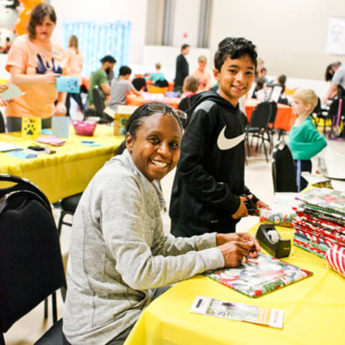Teens and families volunteer together wrapping gifts at a youth volunteer program in Texas.
