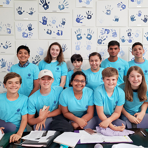 Thirteen teen volunteers in blue shirts pose in a classroom for a Texas youth service program.