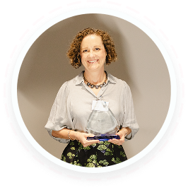 A woman with curly hair smiles holding a volunteer award for youth service programs in Texas.