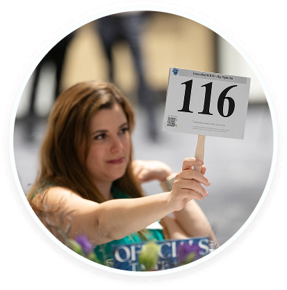 A woman holds up paddle 116 at a youth volunteer auction, promoting teen service programs in Texas.