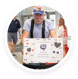 An elderly man with a mustache holds a "GO LICKS!" sign at a youth volunteer event in Texas.