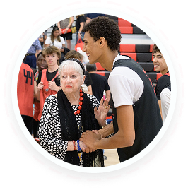 Senior woman and teen volunteer shake hands during youth service program in Texas gym.
