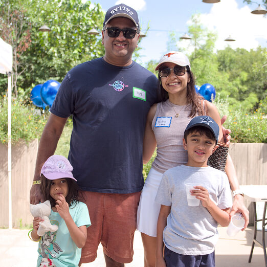 A family in casual summer clothes joins youth volunteer programs Texas outdoors; blue balloons and greenery suggest a volunteering event.