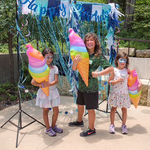 Three children at a youth volunteer event in Texas hold colorful inflatable ice cream cones.