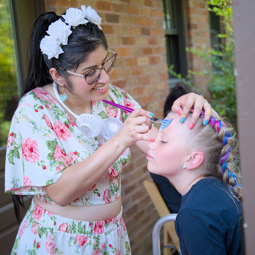 A woman volunteering paints a butterfly on a girl’s forehead at a youth service event in Texas.